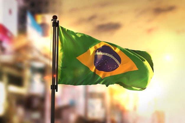 Foto brazilië vlag tegen stad wazige achtergrond bij zonsopgang achtergrondverlichting