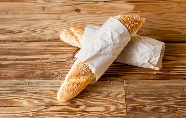 Baguette di pane cosparsa di sesamo e sesamo con carta da imballaggio su un tavolo di legno