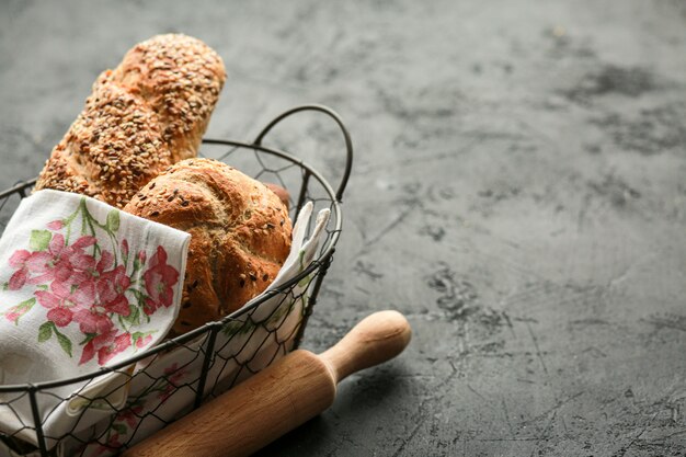 Bread in a basket on a black surface. Assorted bread in a metal basket. Place for recipe and text. Bake bread with a rolling pin and flour. Rye bread, buckwheat rolls and baguette with seeds.