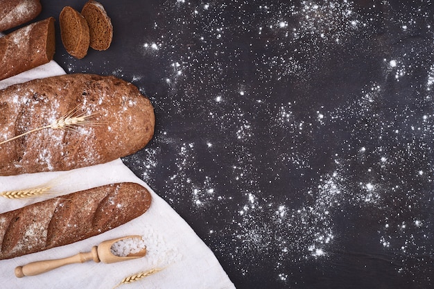 Bread border on wood with copy space background. Brown and white whole grain loaves still life composition with wheat ears scattered around. Bakery and grocery food store concept.