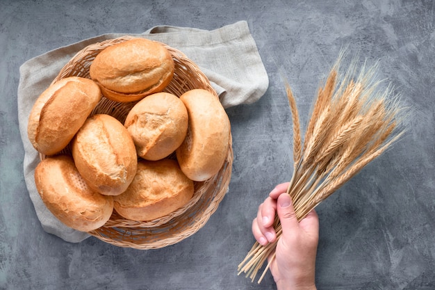 Bread buns in basket on rustic wood with wheat ears, top view on