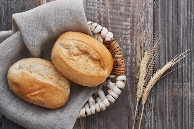 Bread buns in basket on rustic wood with wheat ears