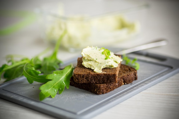 Bread cheese spread with garlic and arugula on dark bread on a wooden table