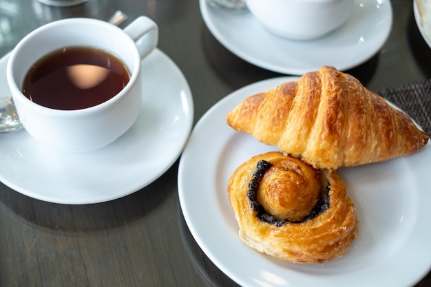 Croissant di pane in un piatto bianco con un bicchiere di tè sul tavolo della colazione