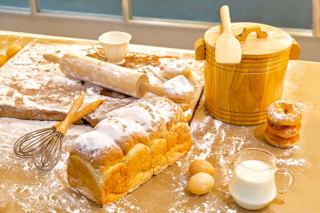 Photo bread, eggs, milk, donuts and fresh milk on wooden table near window. breakfast preparatio