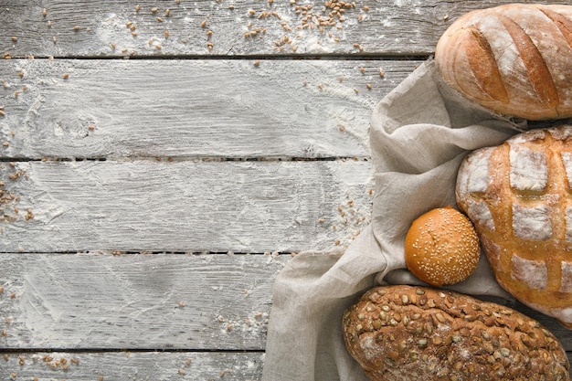 Рамка хлеба на деревенском деревянном фоне, копией пространства. Коричневый и белый хлеб и композиция натюрморта муки с посыпанной пшеничной мукой вокруг.