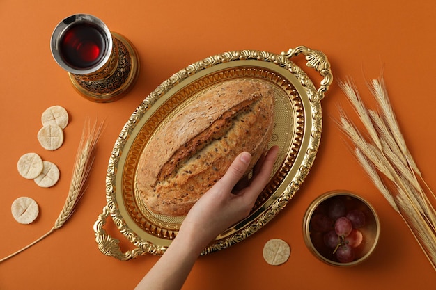Bread on golden tray hand spikelets grapes and cup of wine on orange background top view