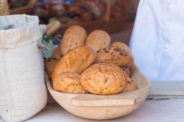 Bread and a lot of fresh buns in a basket on a wooden table next to a linen bag