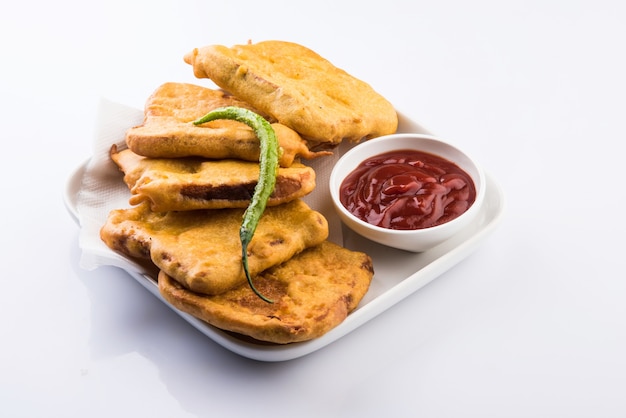 Bread Pakora or pakoda served  with tomato ketchup, green chilly and onion slices, Popular tea-time indian snack. Selective focus