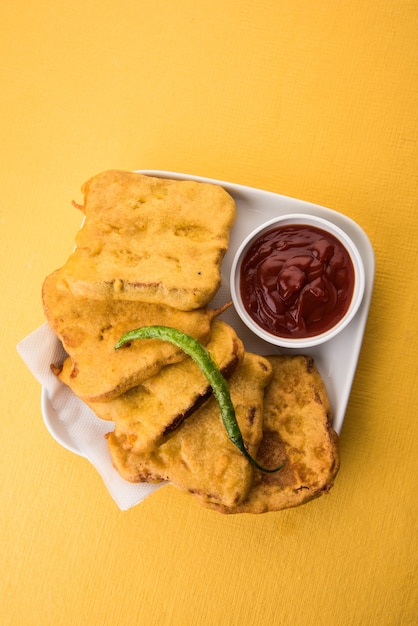 Bread Pakora or pakoda served  with tomato ketchup, green chilly and onion slices, Popular tea-time indian snack. Selective focus