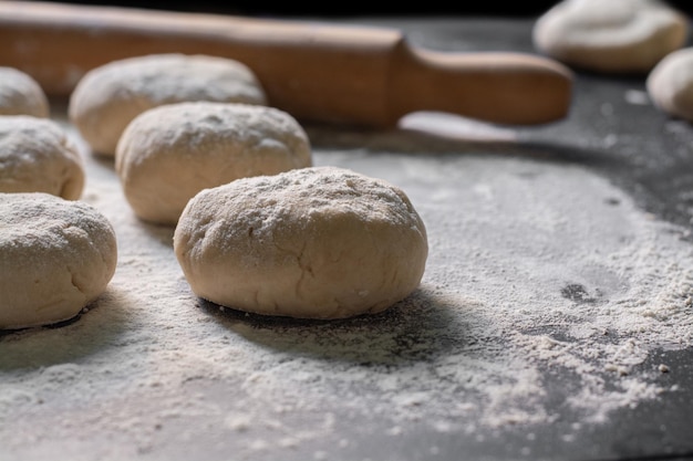 bread and raw flour with n rolling pin on black table