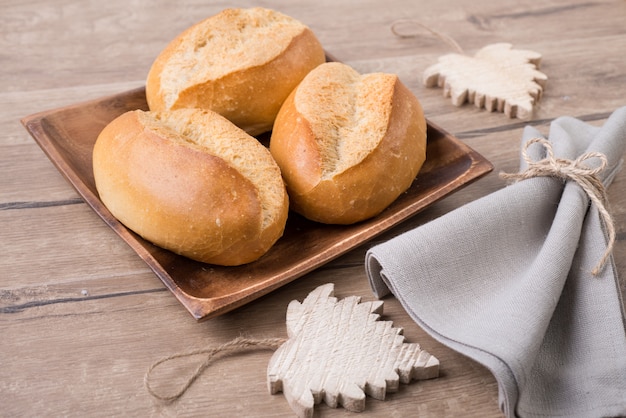 Bread rolls on wooden plate with linen napkin and wooden leaves