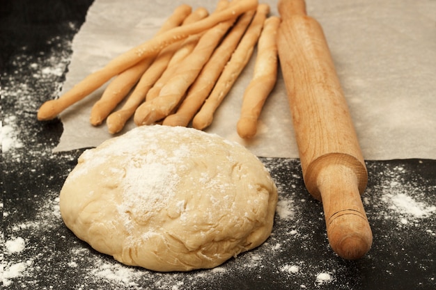 Bread sticks on paper and a piece of dough with a rolling pin