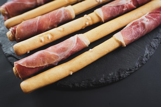 Bread sticks wrapped up by ham on black background