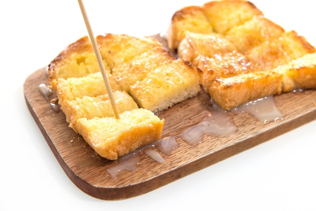 Pane tostato e latte condensato sul piatto di legno su sfondo bianco