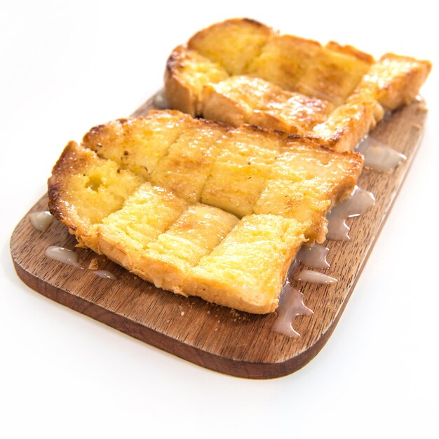 Bread toast and condensed milk on wooden plate over white background