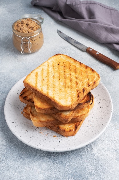 Bread toast crispy for sandwiches on a plate on a gray concrete table. A jar of chicken pate.