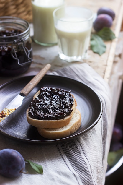 Bread toast with plum jam, served with milk and plums. Rustic style.