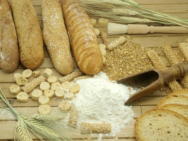 Bread and wheat are on a table with a wooden spoon.