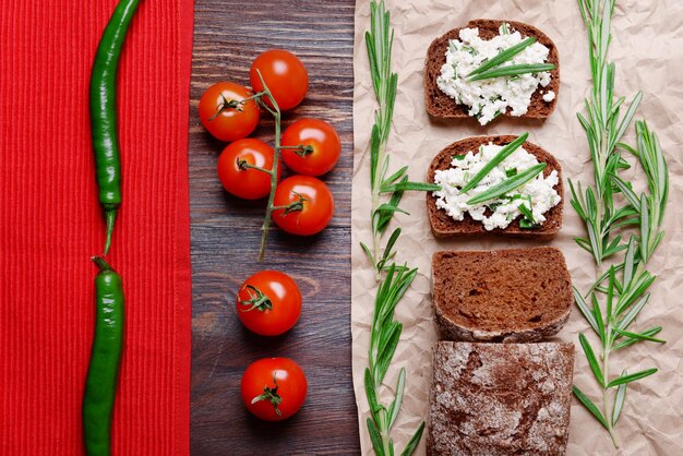 Bread with cottage cheese greens and tomatoes on paper on table top view