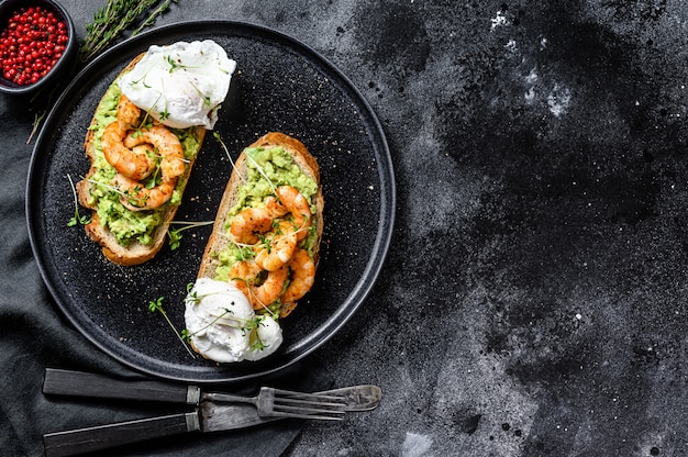 Bread with guacamole, fried shrimp, prawns and egg. Black background. Top view. Copy space