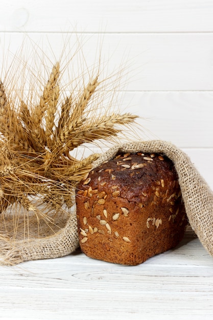 Bread with seeds and wheat ears on wooden table