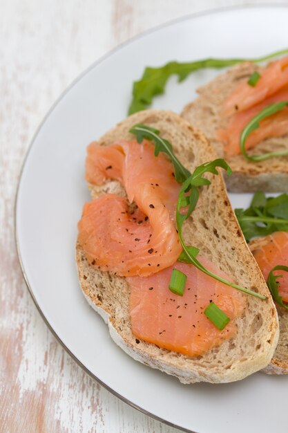 Bread with smoked salmon on white plate on white wooden table