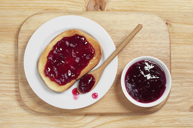 Bread with strawberry jam on cutting board, top view