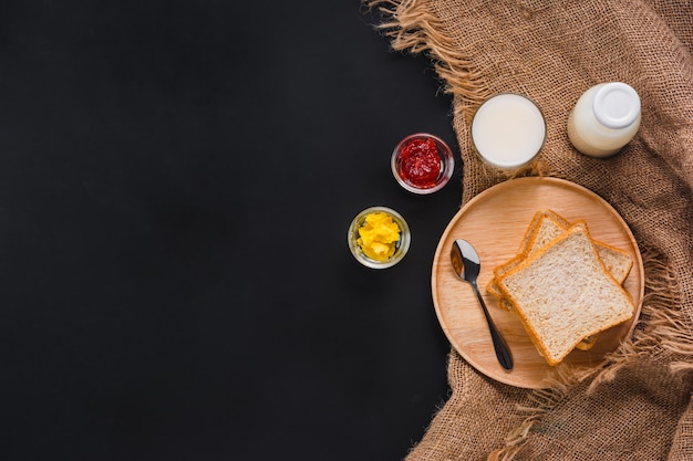 Foto pane con marmellata di fragole, latte e burro su sfondo nero, vista dall'alto