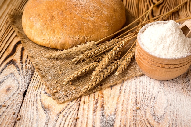 Bread with wheat flour spikes and grains on wooden table Agriculture and harvest concept