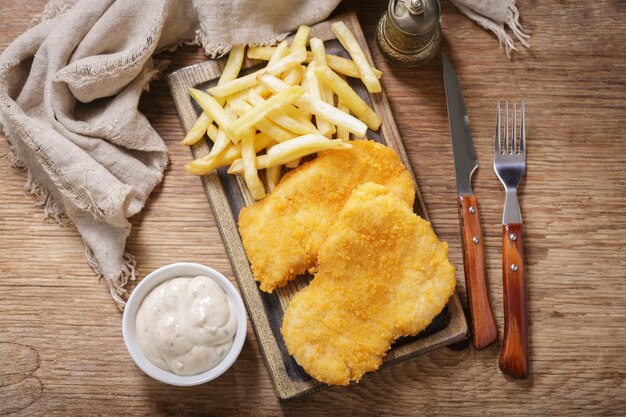 Photo breaded chicken meat or schnitzel with french fries and salad on wooden board