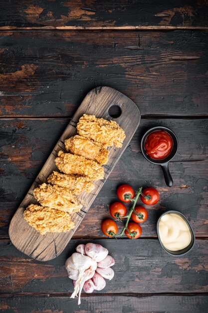 Breaded chicken wings cuts on dark wooden background, flat lay.