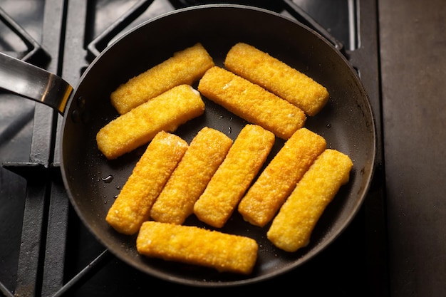 Breaded fish sticks in a frying pan Preparation of frozen fish sticks Fast food Dark background