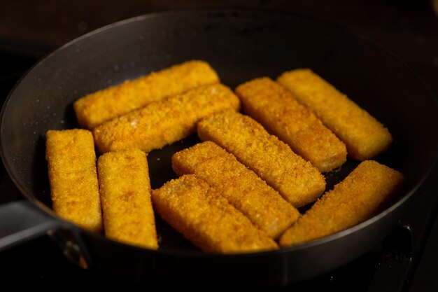 Breaded fish sticks in a frying pan Preparation of frozen fish sticks Fast food Dark background
