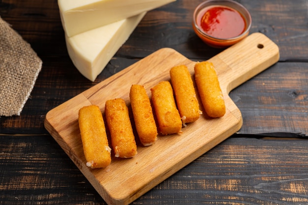 Photo breaded mozzarella cheese sticks with ketchup sauce on wooden cutting board