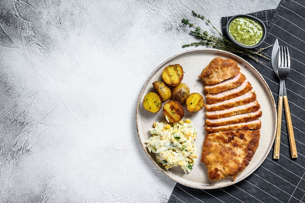 Breaded viennese schnitzel with baked potatoes and salad.  Gray background