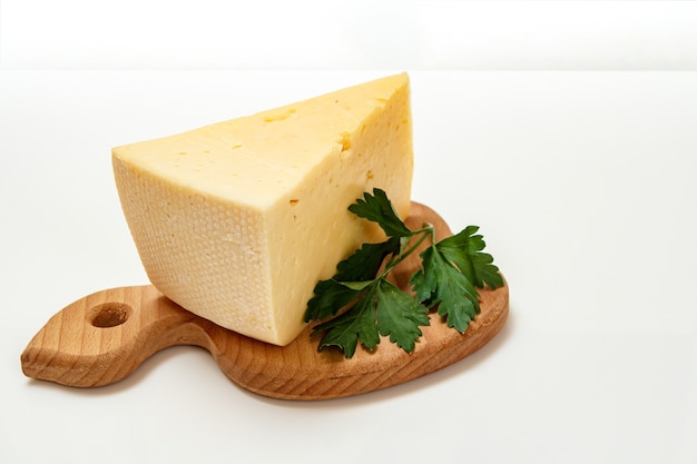 Break of cheese and fresh parsley on a wooden cutting board on the white surface