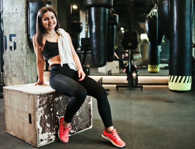 Break time. Smiling fit girl in sportswear sitting on a wooden box in the gym