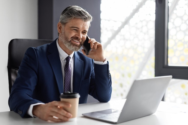 Break at work middle aged businessman talking on cellphone and drinking coffee