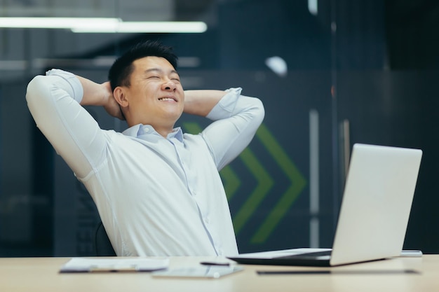 A break at work a young asian man is resting at the workplace at the desk in the office he sits with