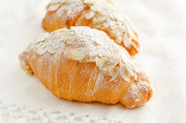 Breakfast bakery, croissant with powdered sugar and almond flakes on white. Close up.