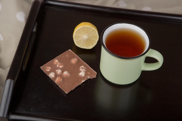 Breakfast in bed - cup of tea, lemon and chocolate on wooden\
tray