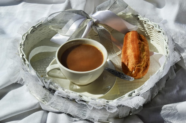 Breakfast in bed in a hotel room morning coffee with cream and\
eclair on white bed linen