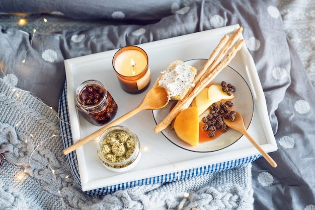 침대에서의 아침 식사, 치즈, 그리 시니, 어린 전나무 콘의 잼 및 양초가 든 쟁반