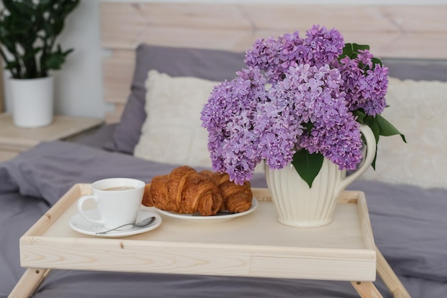 Breakfast in bed Tray with coffee croissants and a bouquet of lilacs on the bed in the bedroom