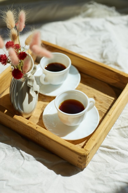 Colazione a letto, prova con due tazze di caffè e fiori alla luce del sole a casa, cameriera che porta vassoio con colazione in camera d'albergo, buon servizio