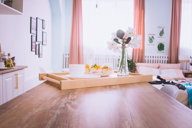 Breakfast in bed with coffee, buns, flowers on wooden tray in hotel bed or at home. Window light