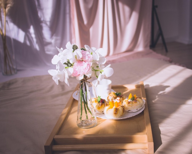 Breakfast in bed with coffee, buns, flowers on wooden tray in\
hotel bed or at home. window light