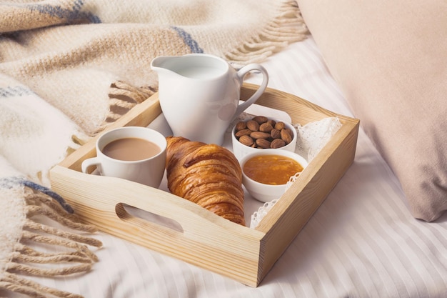 Breakfast in bed with croissant on wooden tray