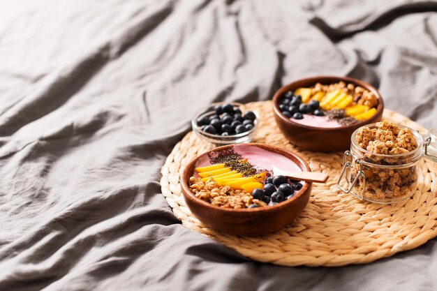 Breakfast on bed with smoothie bowl with granola mango yogurt and blueberry on grey background